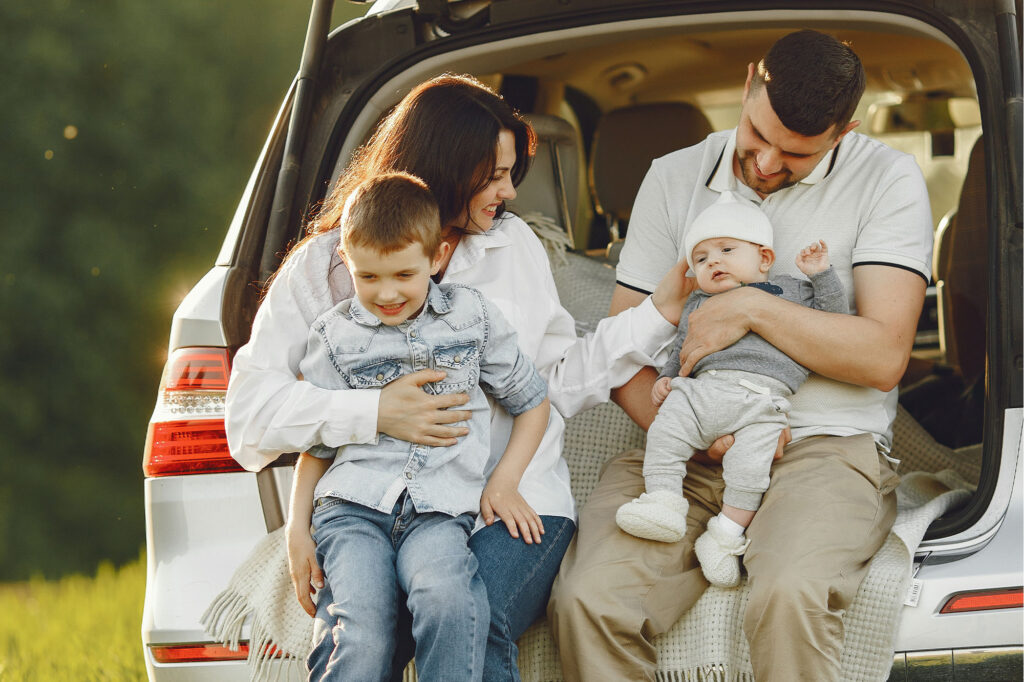 A young couple holds their kids while sitting in the trunk of their SUV