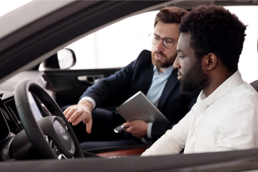 A salesman shows interior features of a used car to a young man