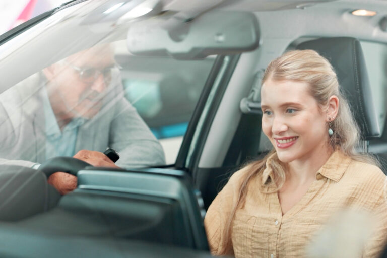 A salesman shows interior features of a used car to a young woman
