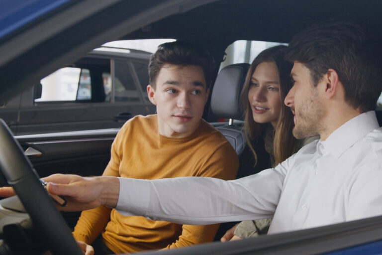A salesman shows interior features of a used car to a young couple