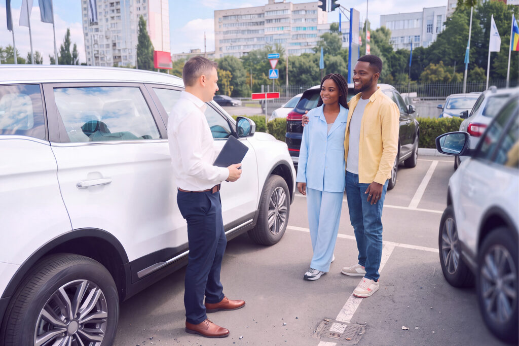 A salesman making a sales pitch to a young couple for used cars
