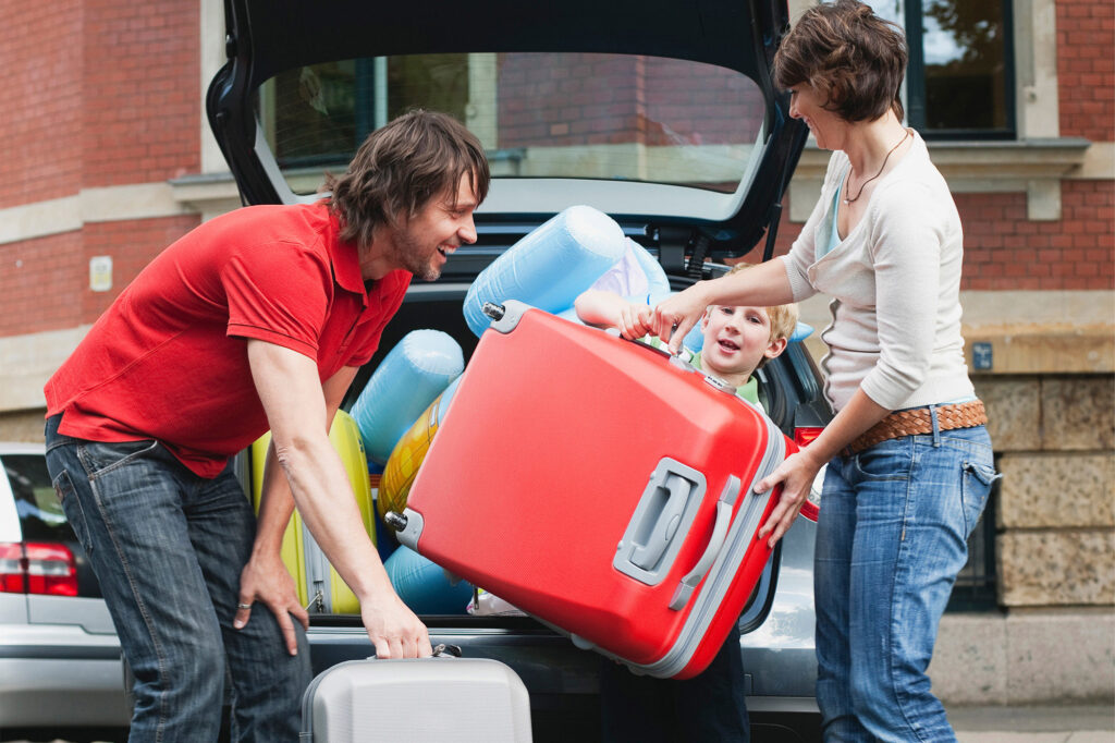 Family loads luggage into a car preparing to go on a road trip