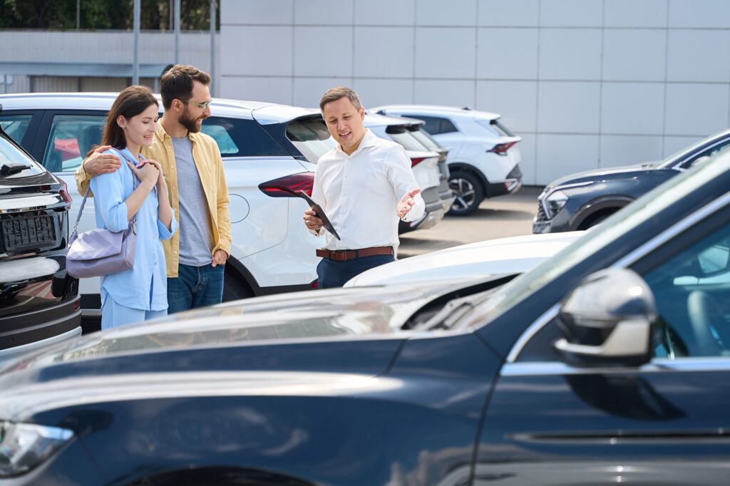 A used cars salesman is showing vehicles to a young couple